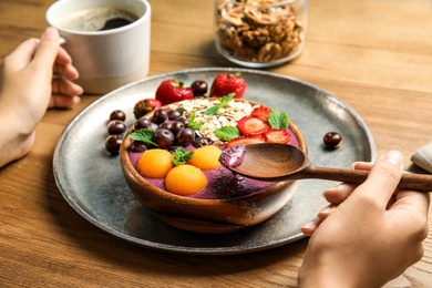 Photo of Woman eating tasty acai smoothie at table, closeup