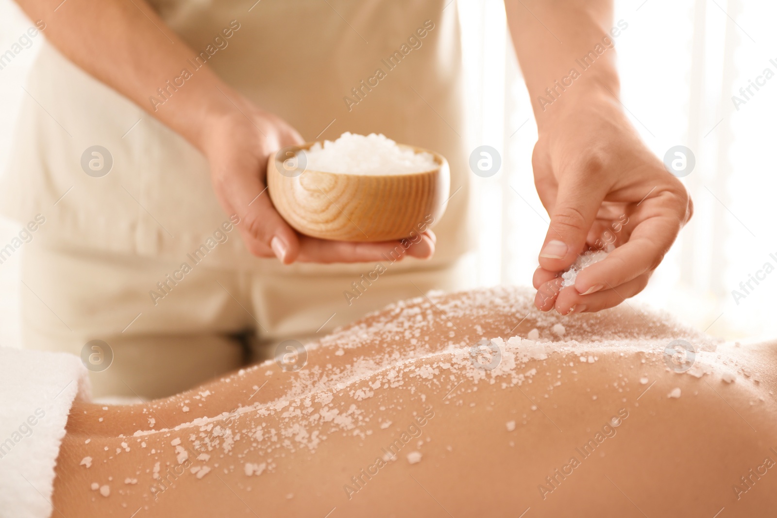 Photo of Young woman having body scrubbing procedure with sea salt in spa salon, closeup