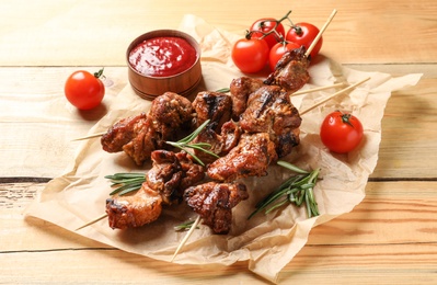 Photo of Delicious barbecued meat served with sauce and garnish on wooden background