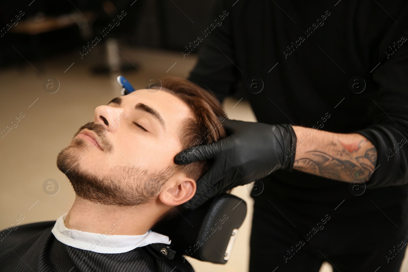 Photo of Professional hairdresser shaving client with straight razor in barbershop