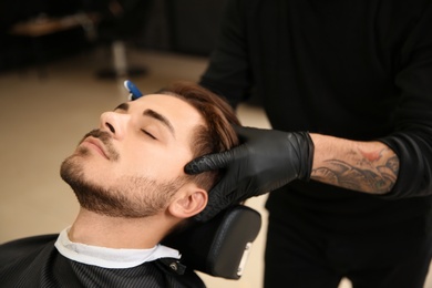 Photo of Professional hairdresser shaving client with straight razor in barbershop