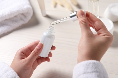 Woman with bottle and pipette of cosmetic serum at white table, closeup