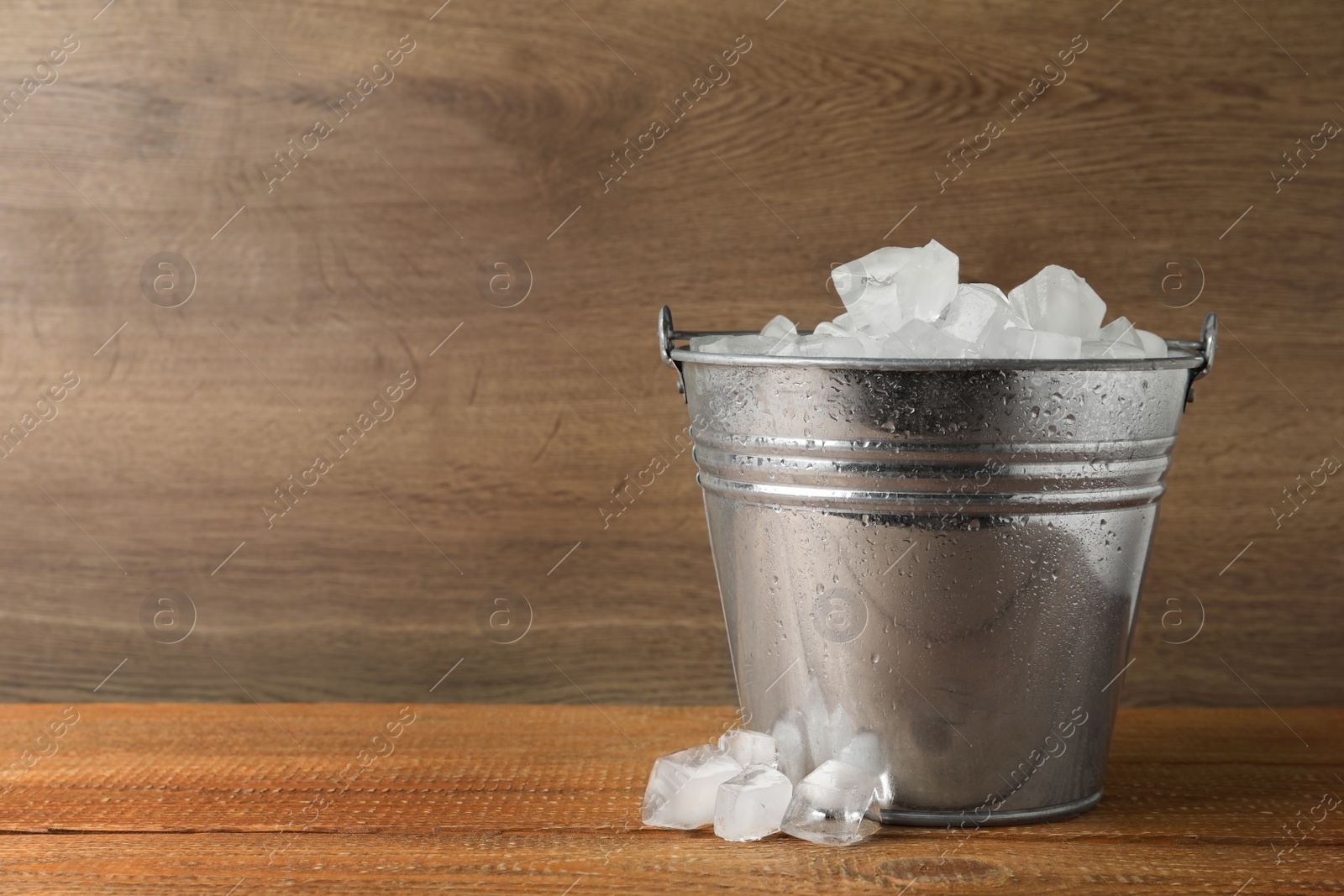 Photo of Metal bucket with ice cubes on wooden background. Space for text