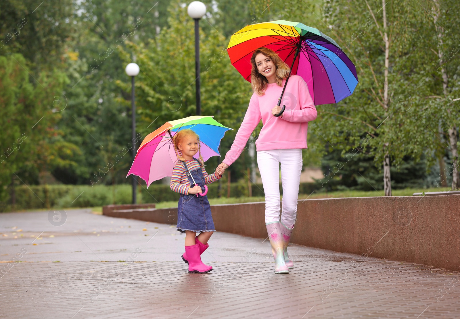 Photo of Happy mother and daughter with bright umbrellas walking in park