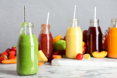 Bottles of delicious juices and fresh fruits on white marble table