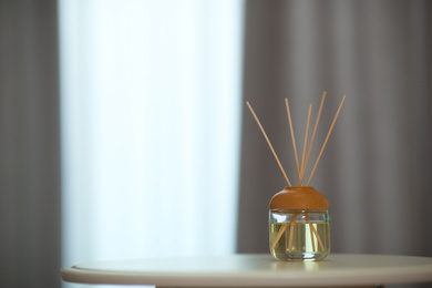 Photo of Aromatic reed air freshener on table indoors. Space for text