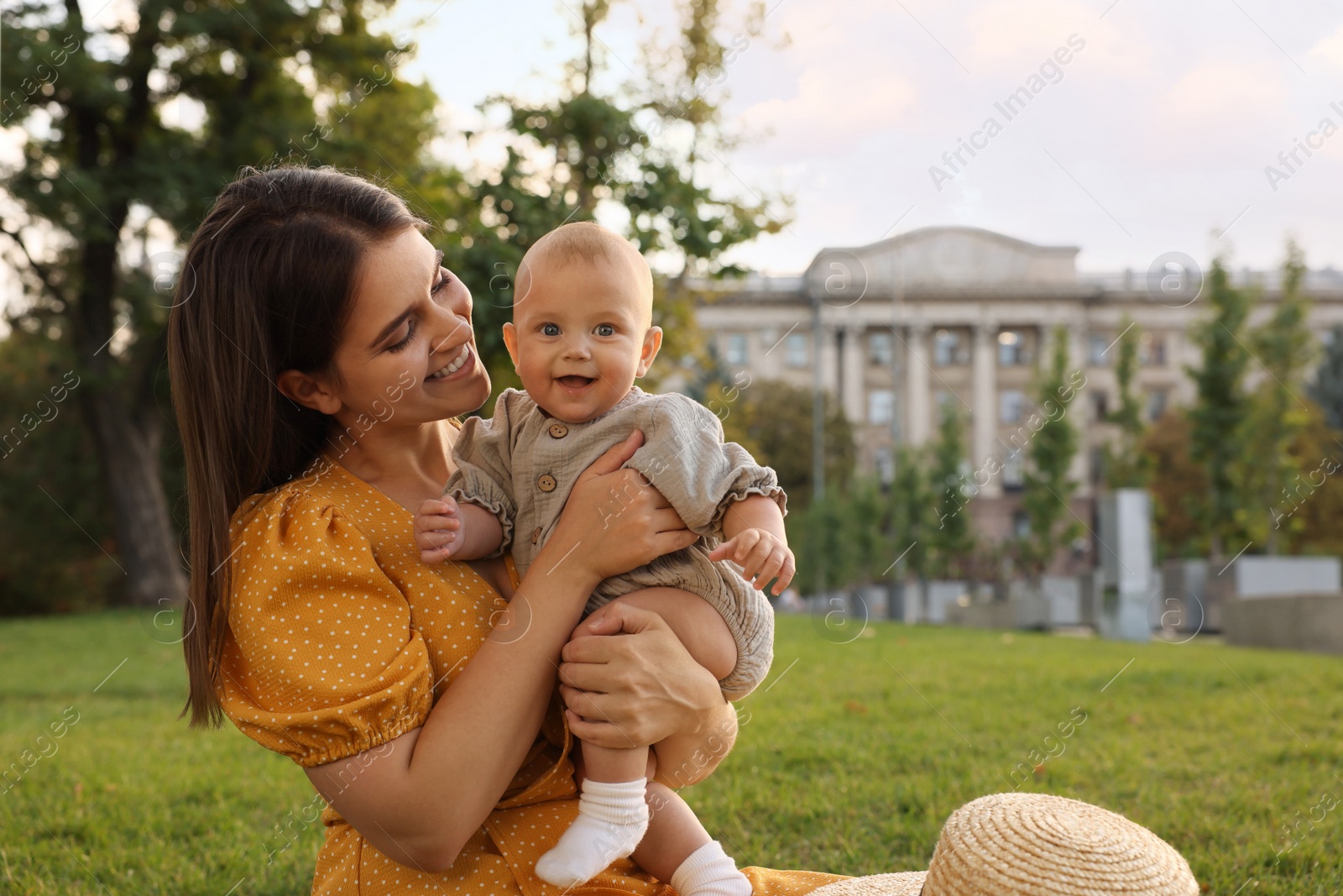 Photo of Happy mother with adorable baby sitting on green grass in park, space for text