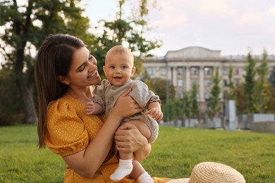 Happy mother with adorable baby sitting on green grass in park, space for text