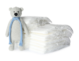 Photo of Disposable diapers and toy bear on white background