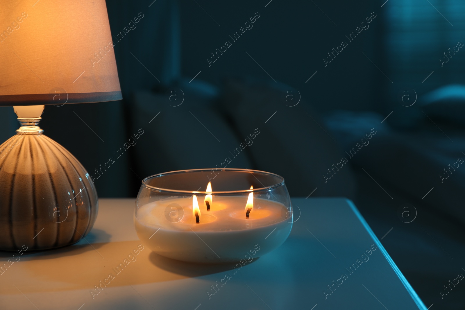 Photo of Burning scented candle and lamp on bedside table in bedroom at night