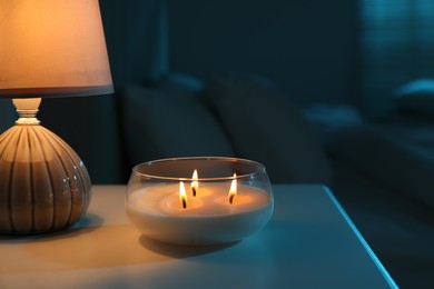 Photo of Burning scented candle and lamp on bedside table in bedroom at night