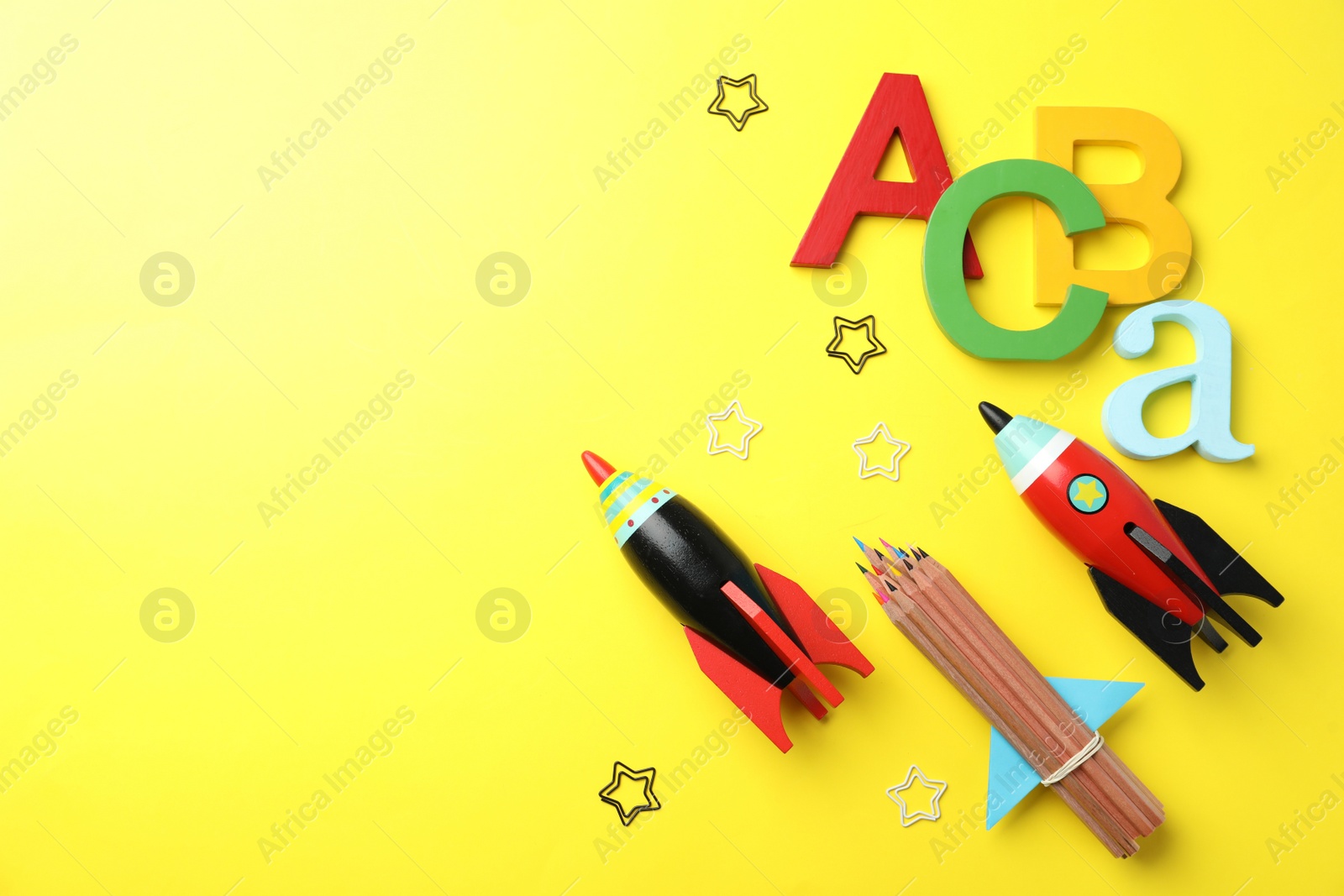 Photo of Bright toy rockets and school supplies on yellow background, flat lay. Space for text