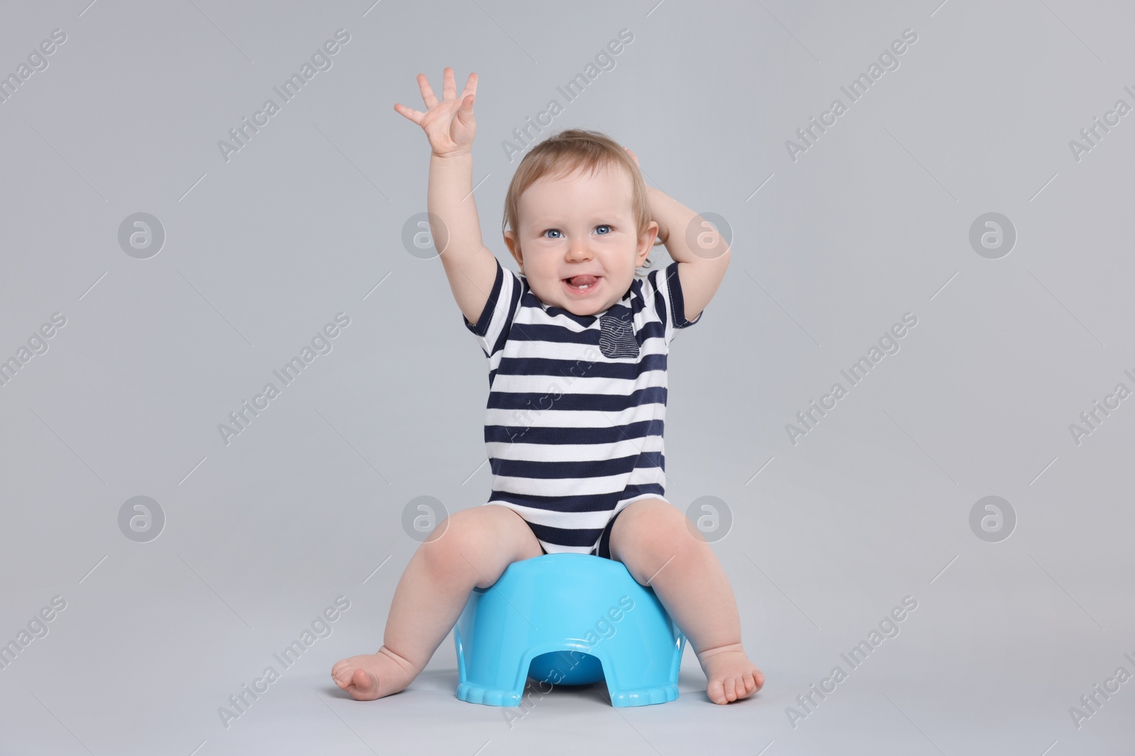 Photo of Little child sitting on baby potty against light grey background