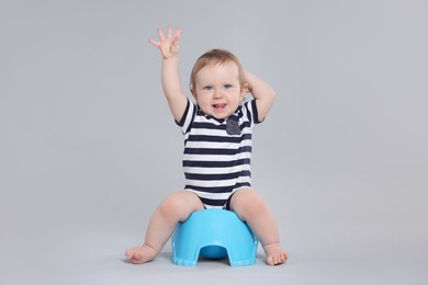 Little child sitting on baby potty against light grey background