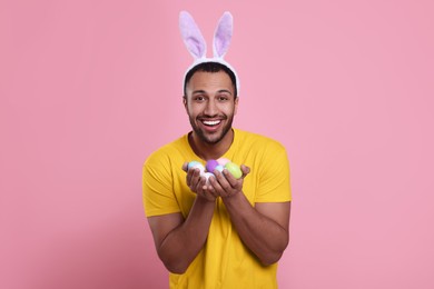 Happy African American man in bunny ears headband with Easter eggs on pink background