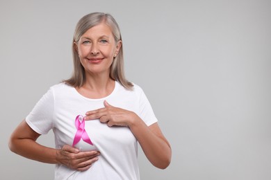 Photo of Beautiful senior woman with pink ribbon on light grey background, space for text. Breast cancer awareness