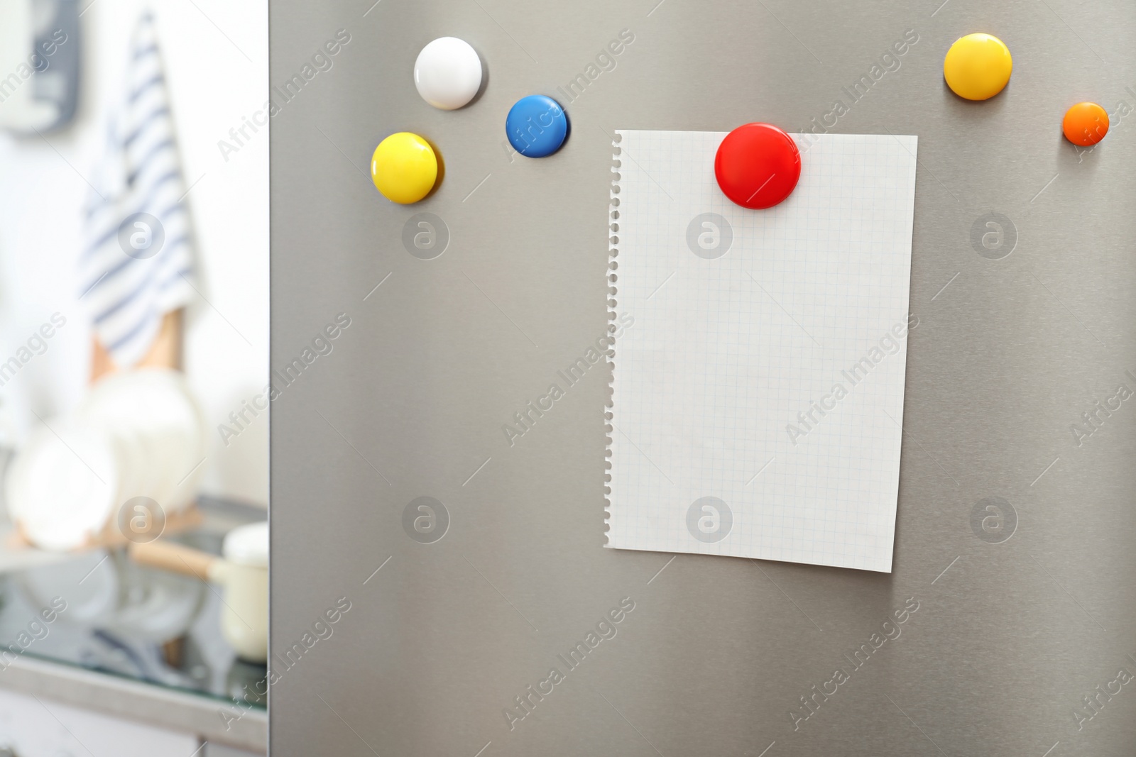 Photo of Empty sheet of paper with colorful magnets on refrigerator door in kitchen. Space for text