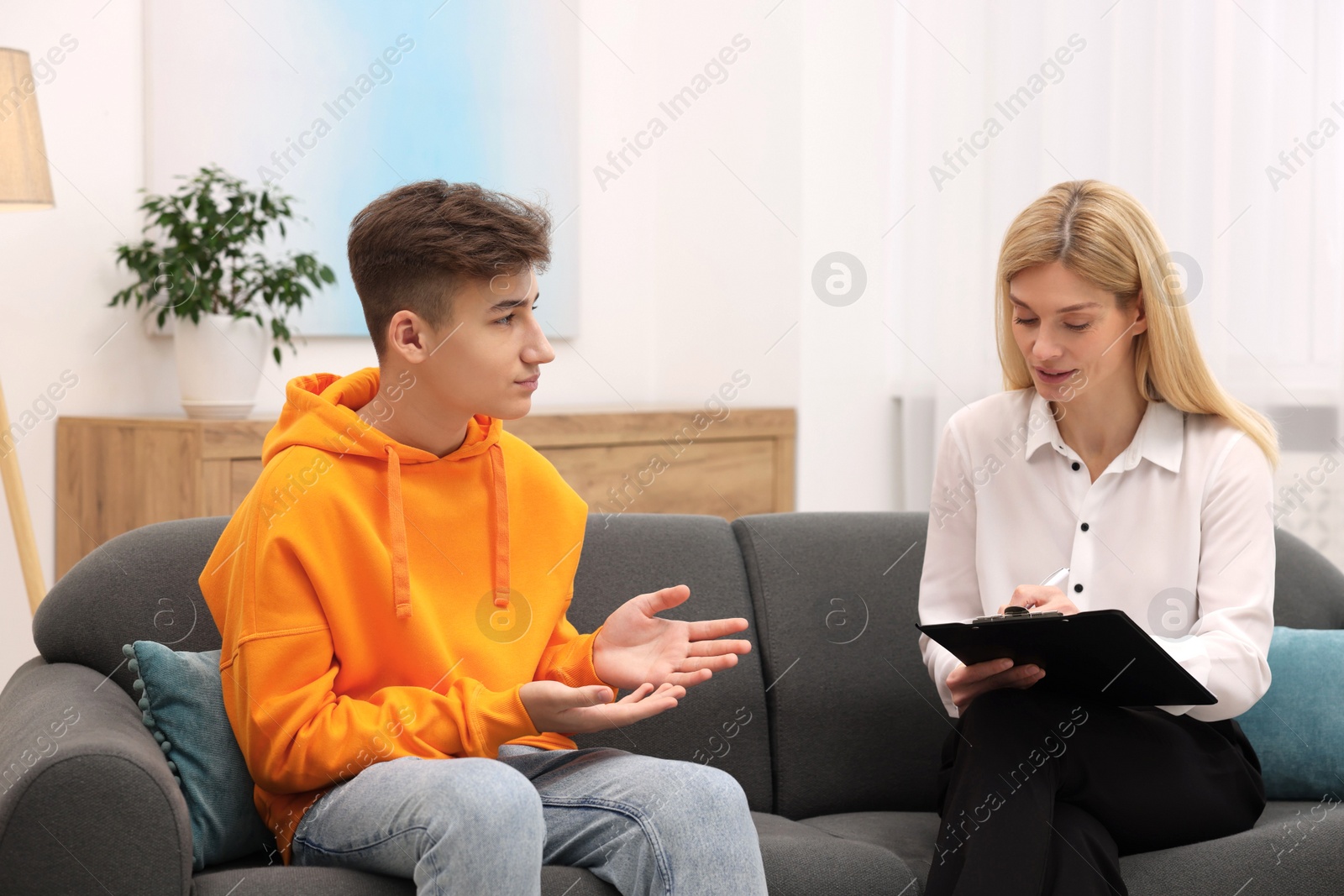 Photo of Psychologist working with teenage boy on sofa in office