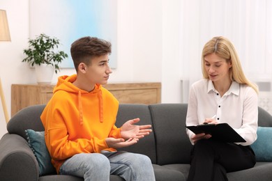 Psychologist working with teenage boy on sofa in office