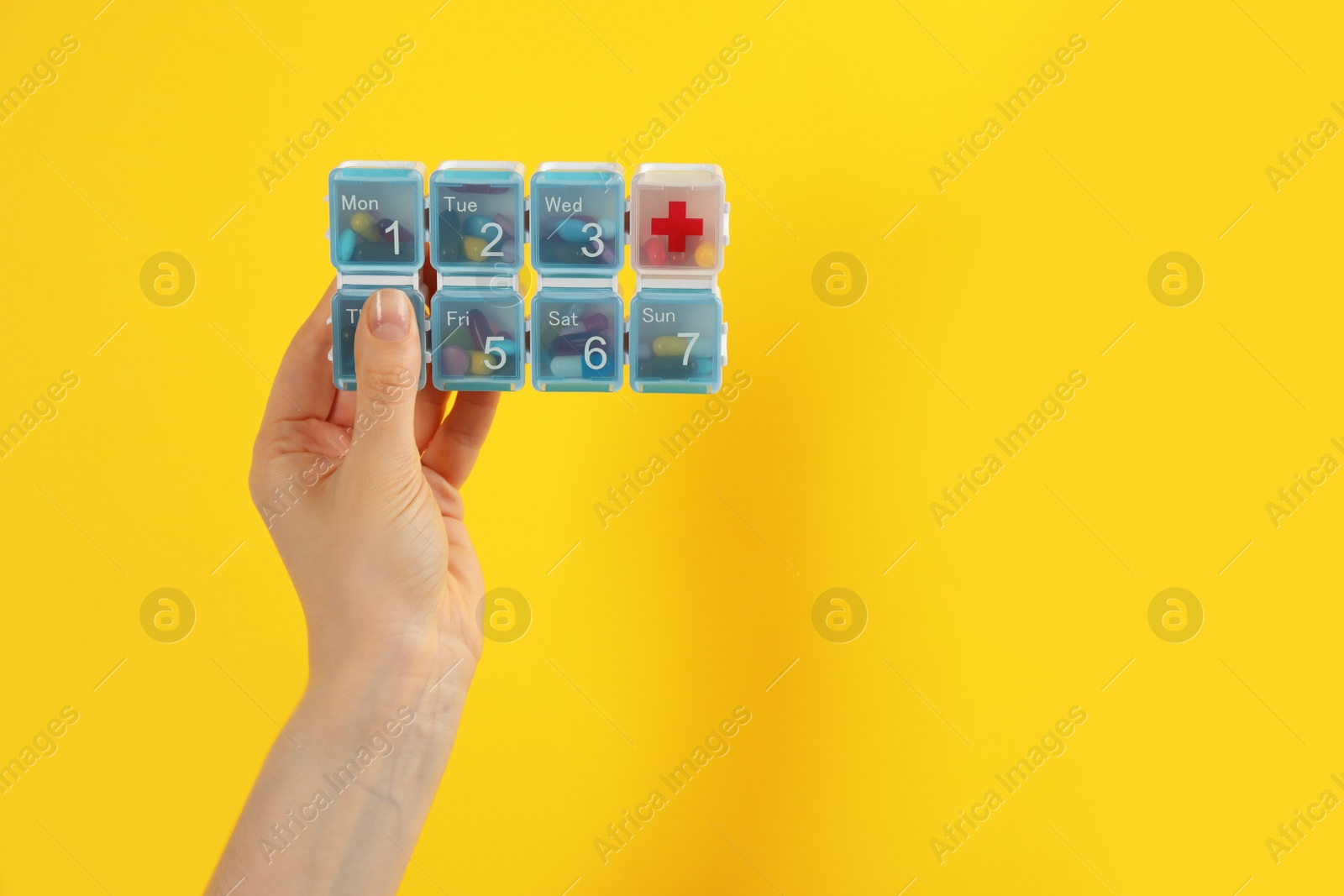 Photo of Woman holding plastic box with different pills on yellow background, closeup. Space for text