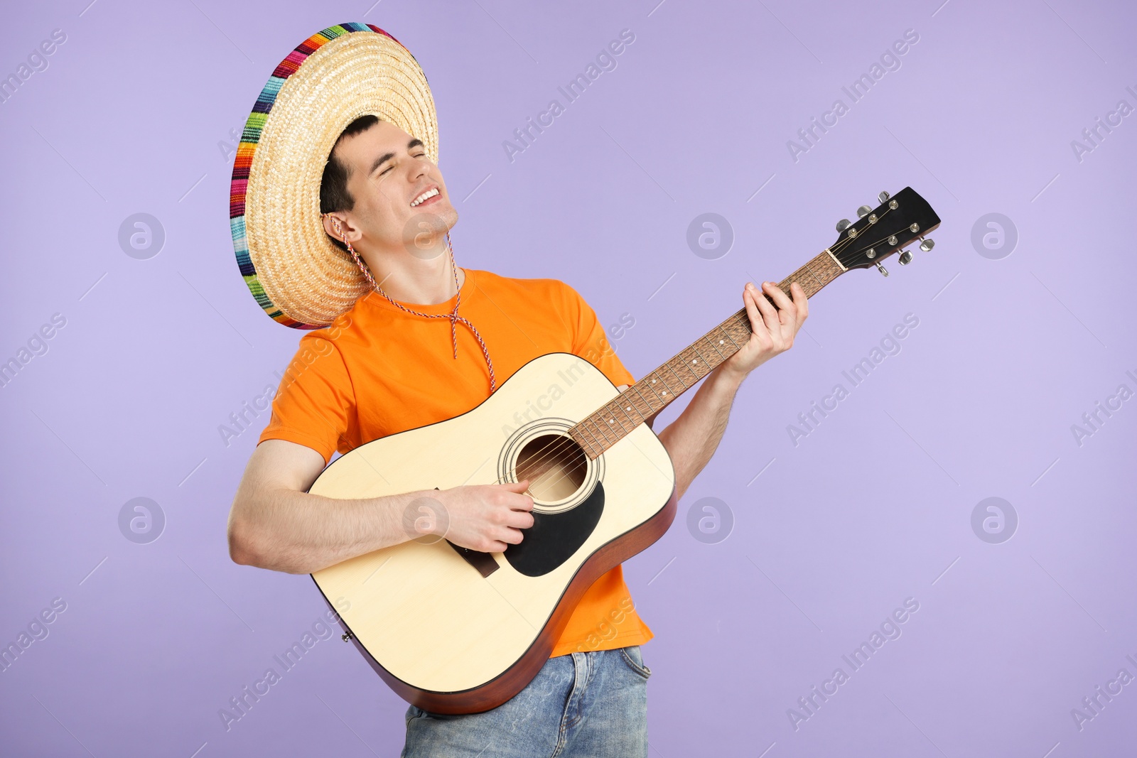 Photo of Young man in Mexican sombrero hat playing guitar on violet background