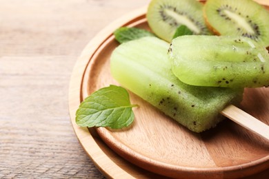 Photo of Plate of tasty kiwi ice pops on wooden table, closeup. Fruit popsicle