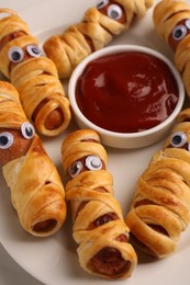 Photo of Plate with tasty sausage mummies for Halloween party and ketchup on table, closeup