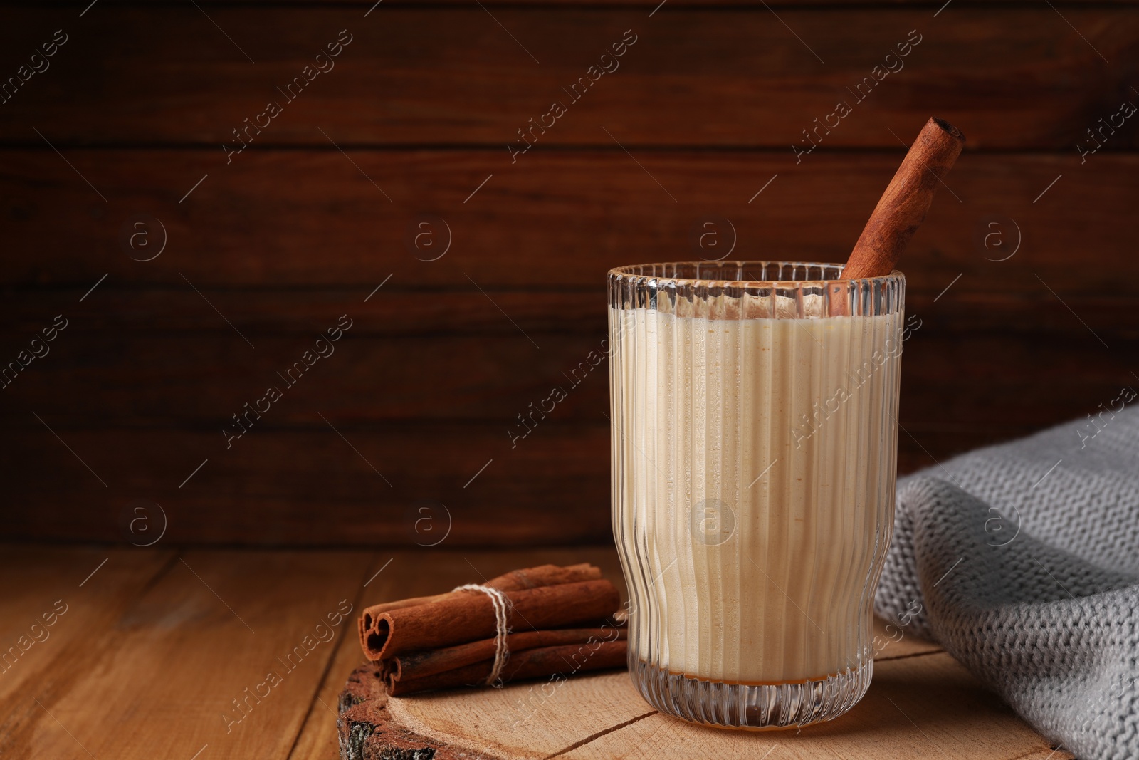 Photo of Glass of delicious eggnog with cinnamon on wooden table, space for text