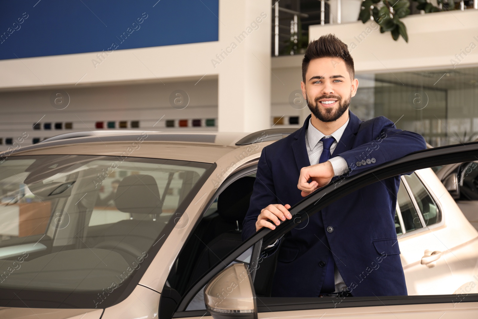 Photo of Young salesman near new car in dealership