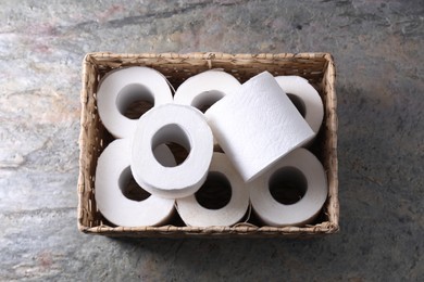 Photo of Toilet paper rolls in wicker basket on textured table, top view