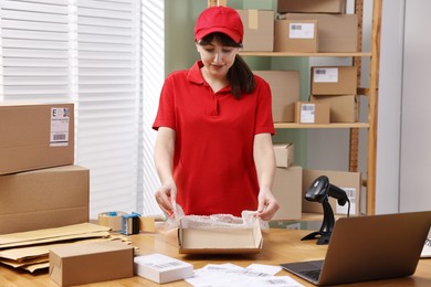 Photo of Post office worker packing parcel at wooden table indoors