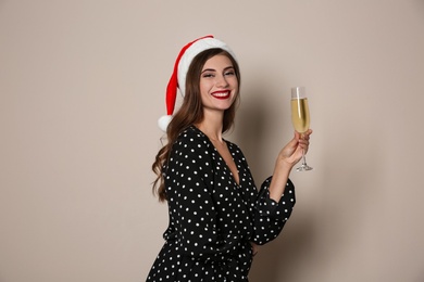 Photo of Happy woman in Santa hat with champagne on beige background. Christmas party