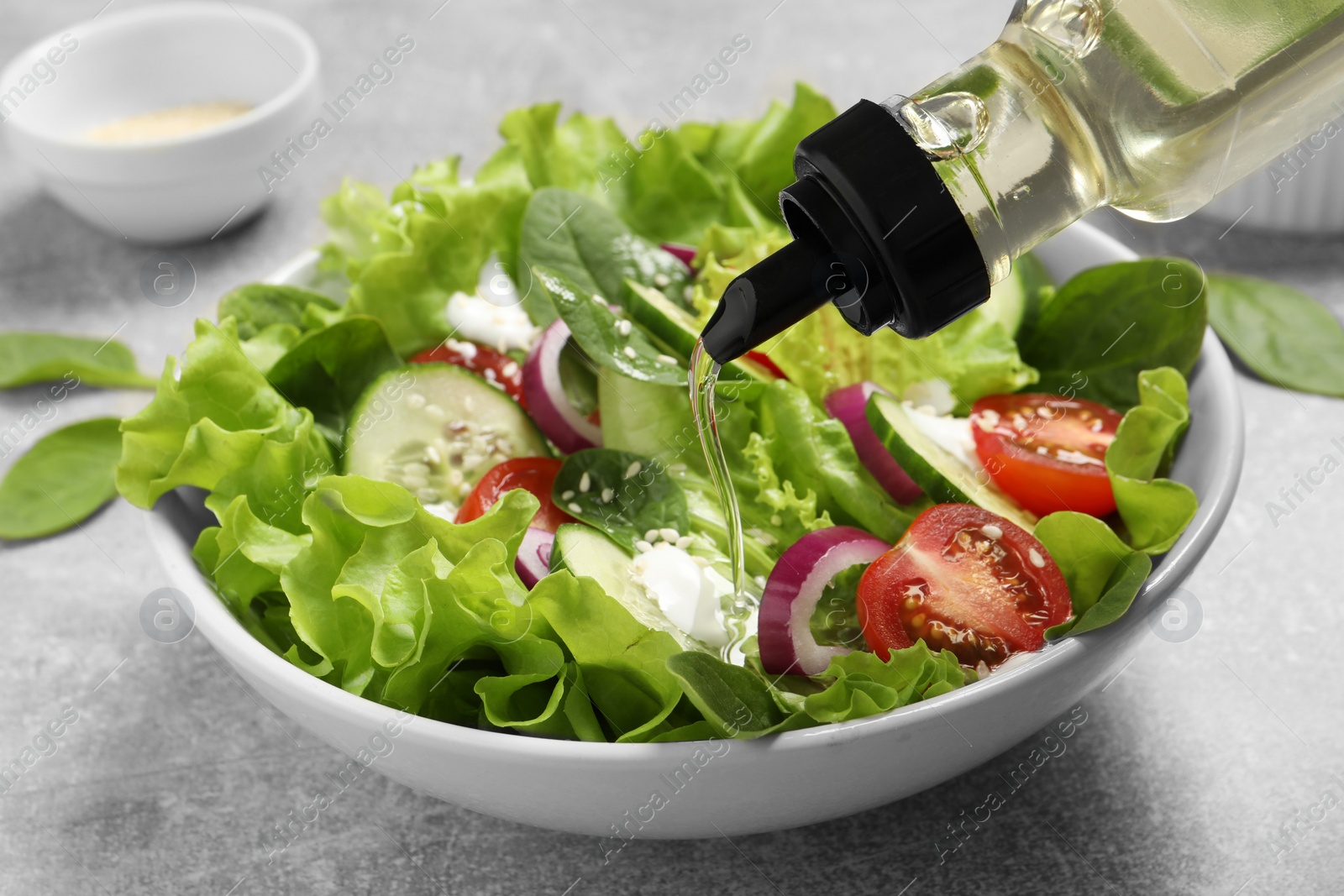 Photo of Pouring oil into delicious salad on light grey table, closeup