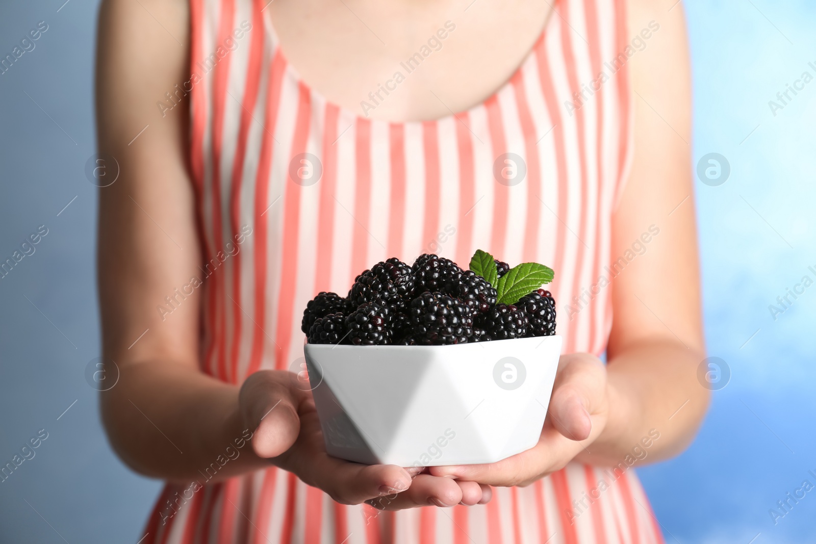 Photo of Woman holding bowl of fresh blackberry against color background, closeup