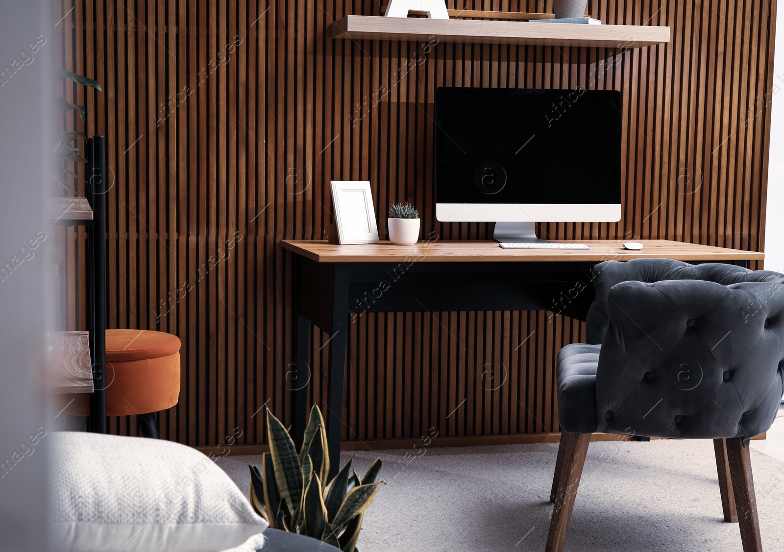 Photo of Comfortable workplace with computer near wooden wall in stylish room interior. Home office design