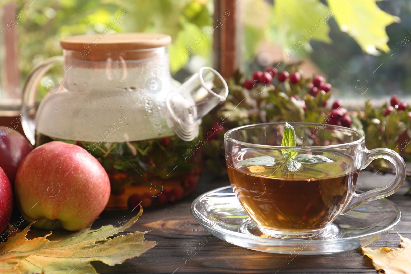 Photo of Hot tea, apples and dry leaves on wooden windowsill. Autumn atmosphere