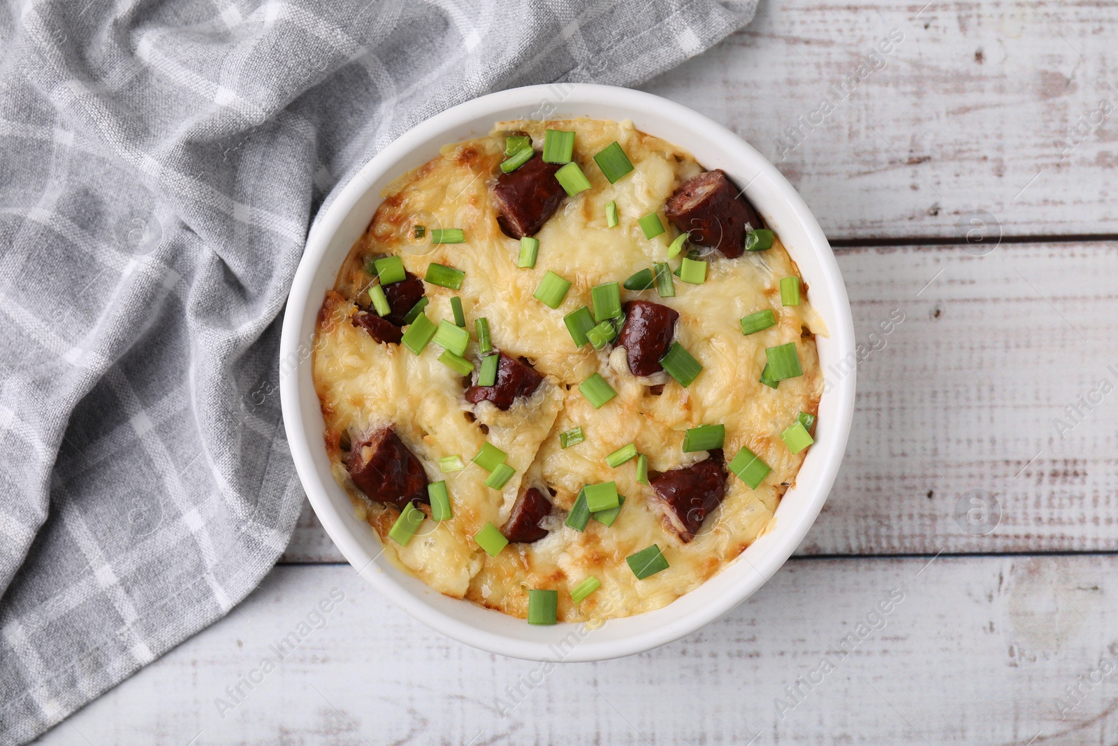 Photo of Tasty sausage casserole with green onion in baking dish on white wooden table, top view