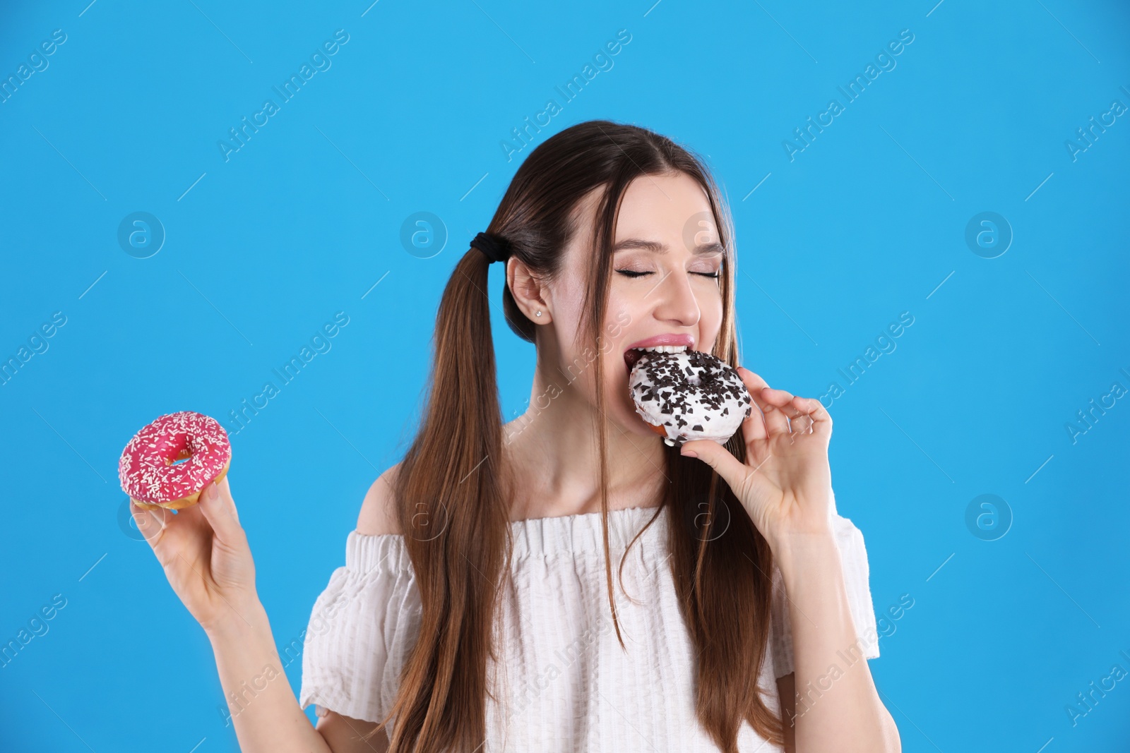 Photo of Beautiful young woman with donuts on light blue background