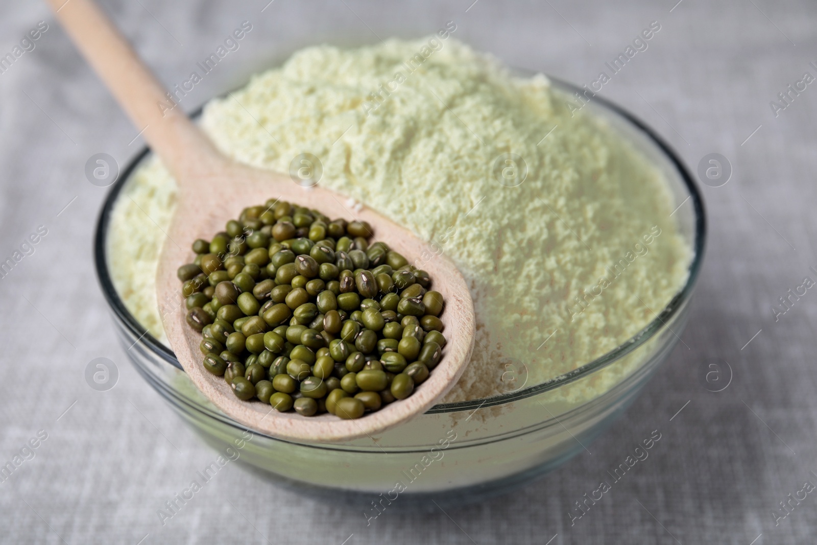 Photo of Bowl of flour, spoon and mung beans on light grey cloth, closeup