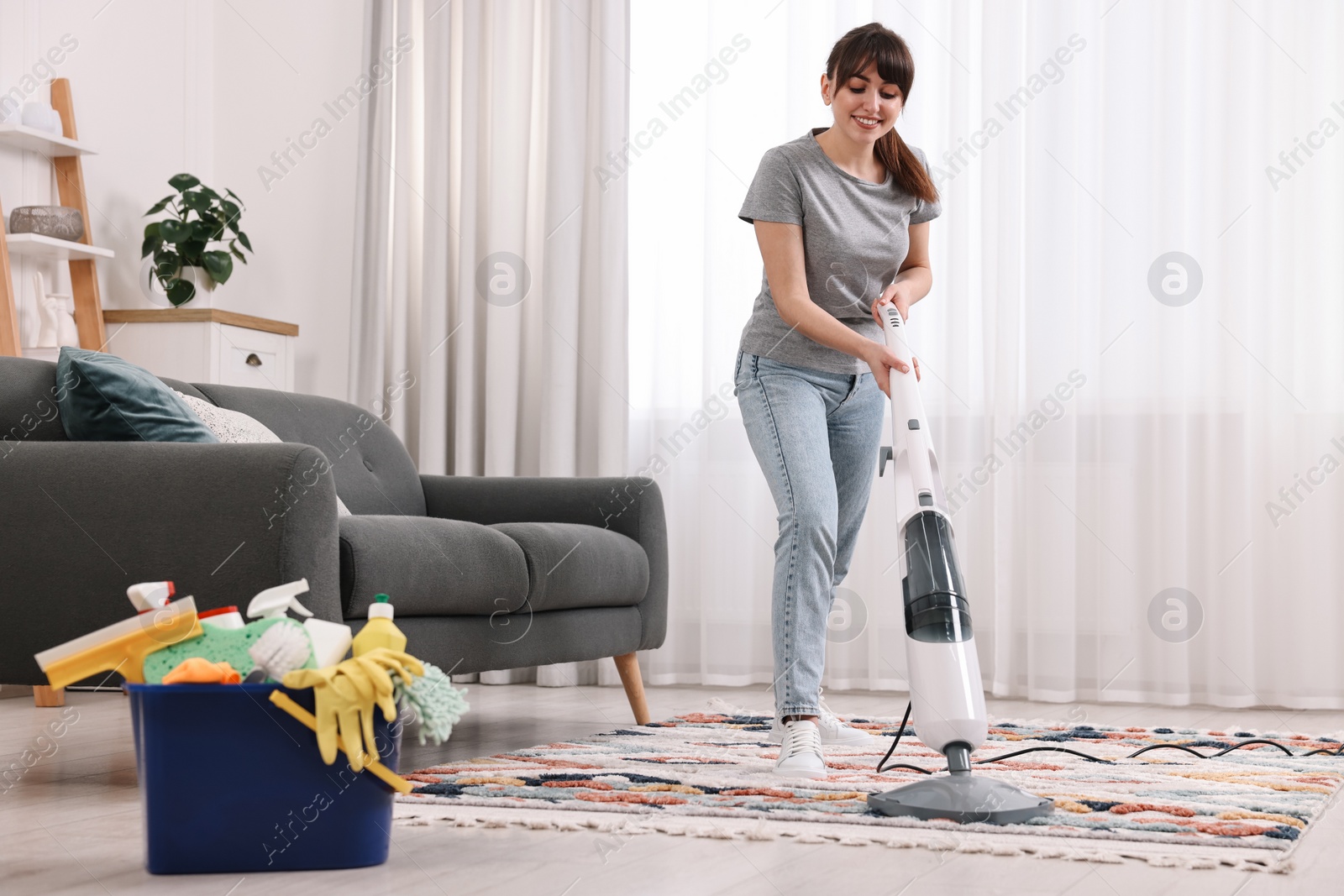 Photo of Happy young housewife vacuuming rug at home