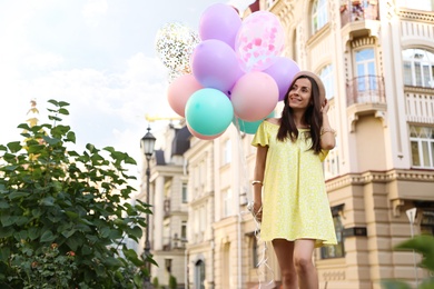 Photo of Beautiful young woman with color balloons on city street