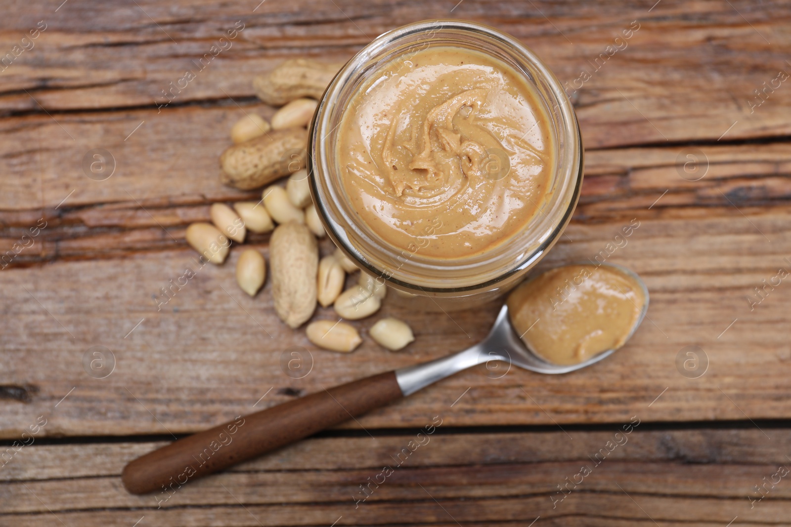 Photo of Tasty peanut nut paste in jar and spoon on wooden table, flat lay