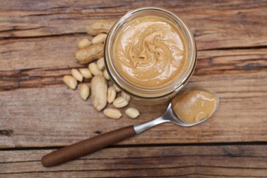 Tasty peanut nut paste in jar and spoon on wooden table, flat lay