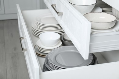 Open drawers with different plates and bowls in kitchen, closeup