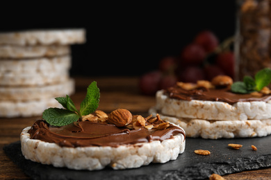 Photo of Puffed rice cakes with chocolate spread, nuts and mint on slate board, closeup