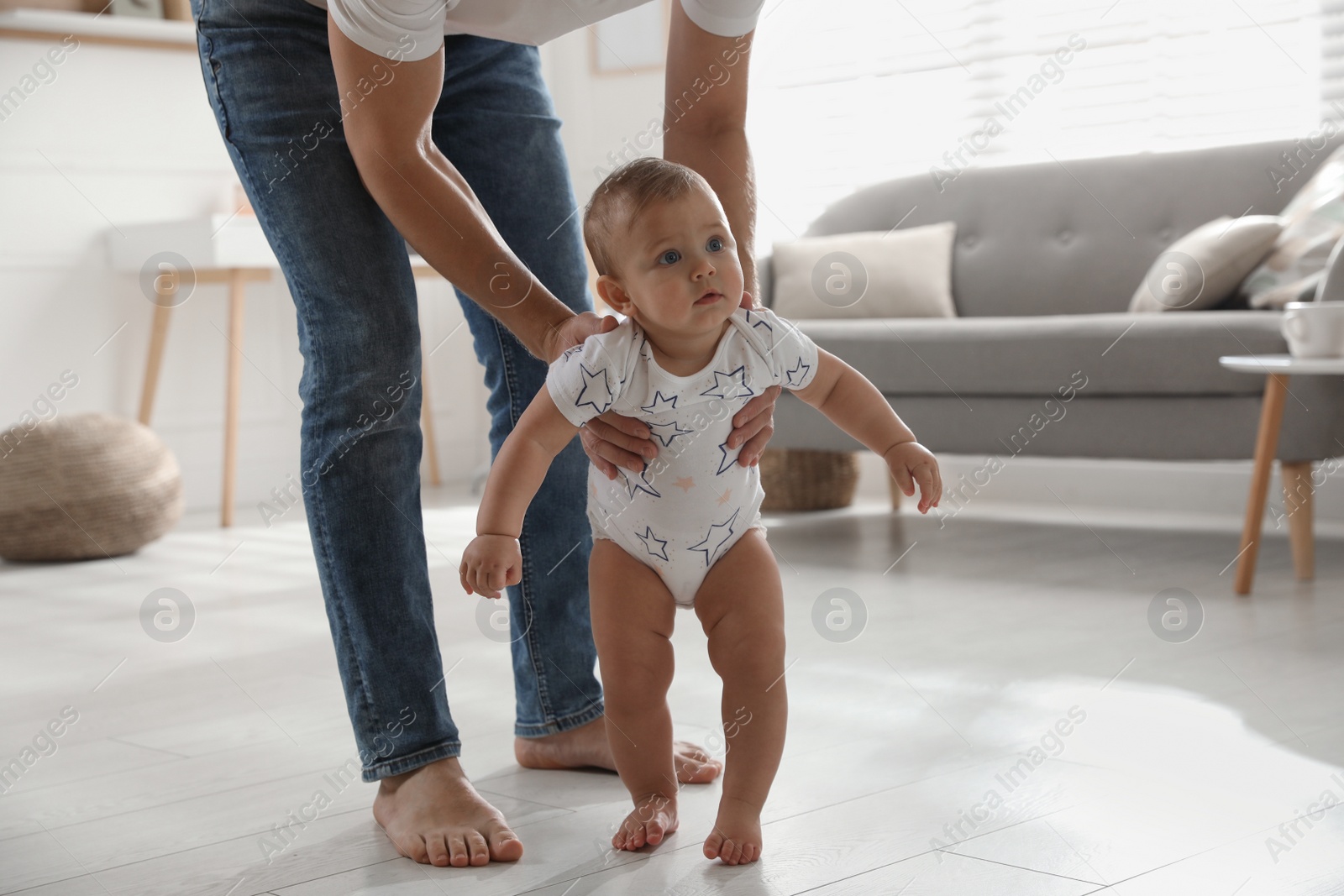 Photo of Father supporting his baby daughter while she learning to walk at home