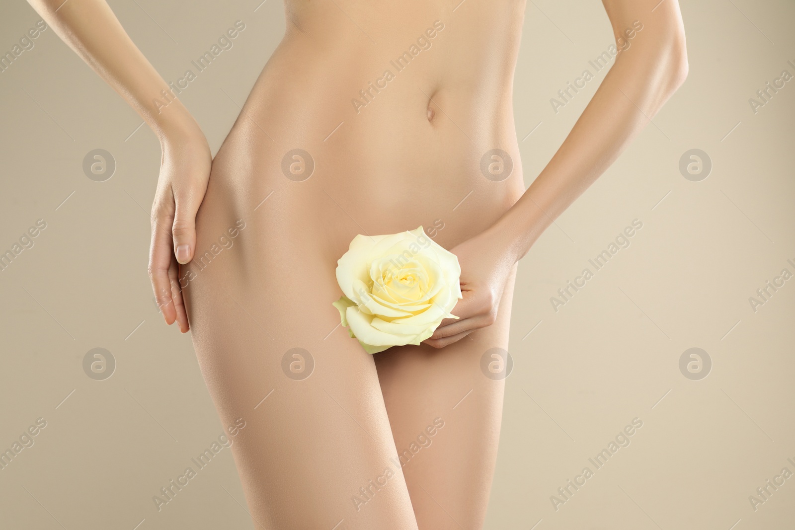 Photo of Woman with flower showing smooth skin after Brazilian bikini epilation on beige background, closeup. Body care concept