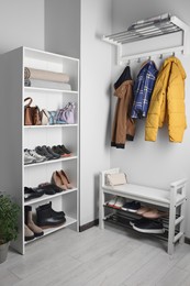 Shelving unit, coat rack and shoe storage bench near white wall in hallway. Interior design
