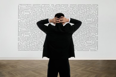 Businessman looking at wall with illustration of maze indoors