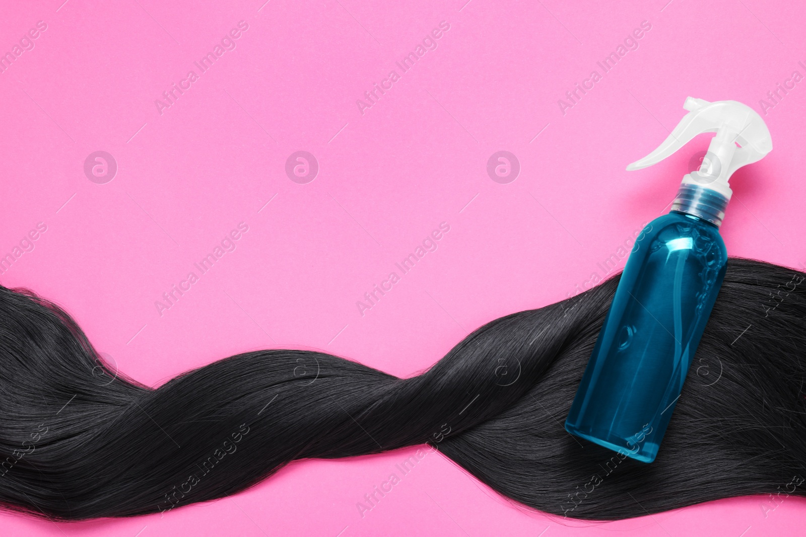 Photo of Spray bottle with thermal protection and lock of brunette hair on pink background, flat lay. Space for text